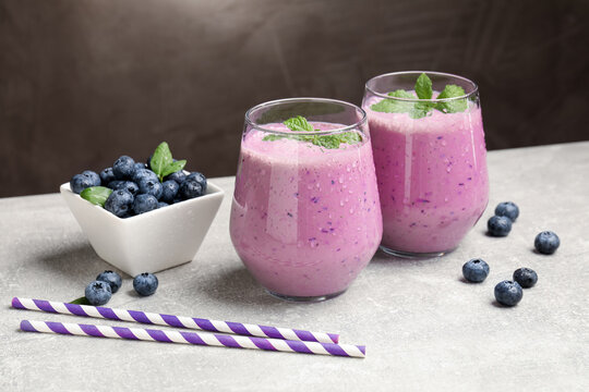Tasty smoothie in glasses, fresh blueberries, straws and mint on grey table, closeup