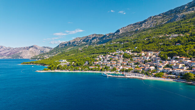 Aerial view of Brela town on the Makarska Riviera in Croatia, featuring a scenic coastline with turquoise sea, pebble beaches, and pine forests at the foot of the Biokovo mountains