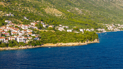 Fototapeta premium Scenic coastal village with white houses and red roofs nestled on a green hillside by the Adriatic Sea in Croatia