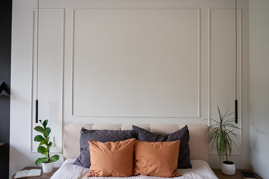 Modern bedroom interior with bed, pillows, indoor plants and pendant lights against wall molding