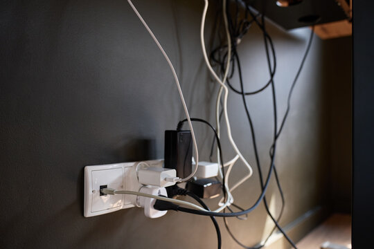 Close up of wall outlet with connected adapters, plugs and tangled cables