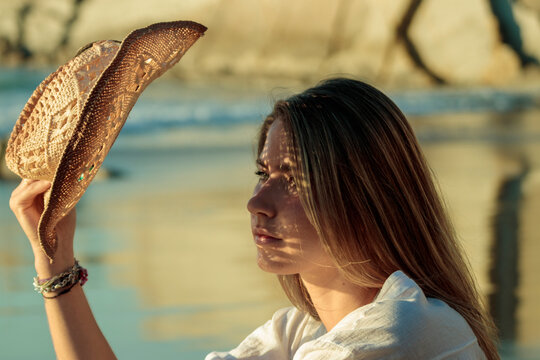 Woman holding straw hat reflecting sunlight at beach