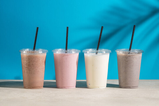 Four iced milkshake cups with straws on blue backdrop