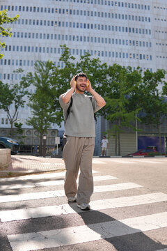 Happy man with headphones crossing city street in sunlight