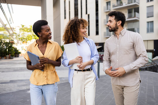 Diverse coworkers walking and talking in modern city street