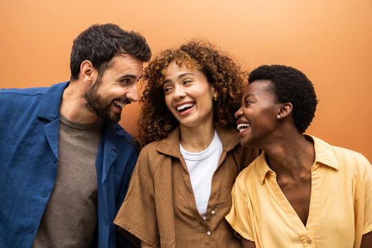 Joyful friends laughing together against warm studio backdrop