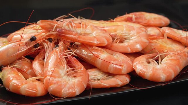 Detailed macro shot of freshly cooked Vietnamese whiteleg shrimp rotating on a dark plate.