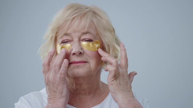 An elderly woman applies eye patches to enhance her beauty while prioritizing selfcare