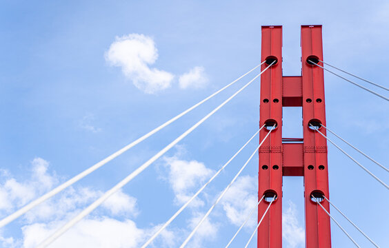 Red suspension bridge tower and cables against blue sky