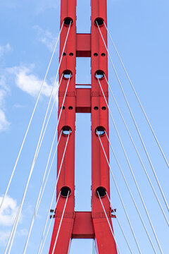 Red suspension bridge tower with steel cable lines in sky
