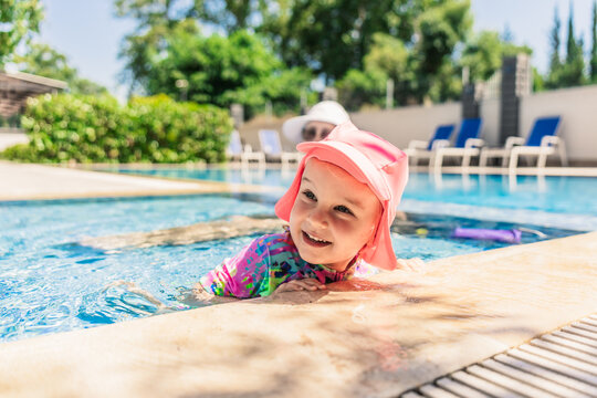 Happy child in sun hat swimming in outdoor resort pool