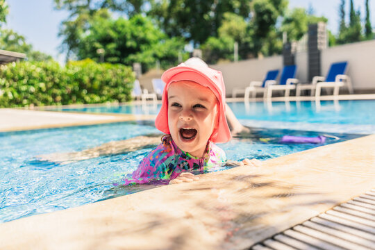 Happy child in sun hat playing at outdoor swimming pool