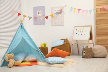 Beautiful wigwam with soft pillows, toys and magnetic board in child's room © New Africa