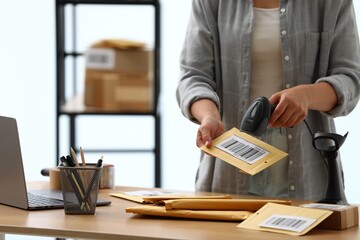 Post office worker with scanner reading barcode on envelope at wooden desk indoors, closeup. Space for text © New Africa