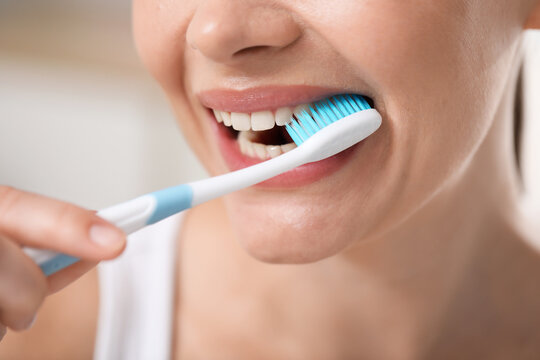 Woman brushing her teeth with toothbrush indoors, closeup