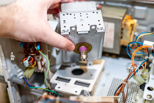 Installing a magnetron during microwave oven repair. The metal housing, wiring, and circuit board components surround the part