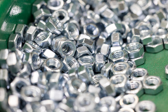 Close up view of many small metal hex nuts in green industrial sorting machine tray. Professional hardware parts for construction and engineering industries background.