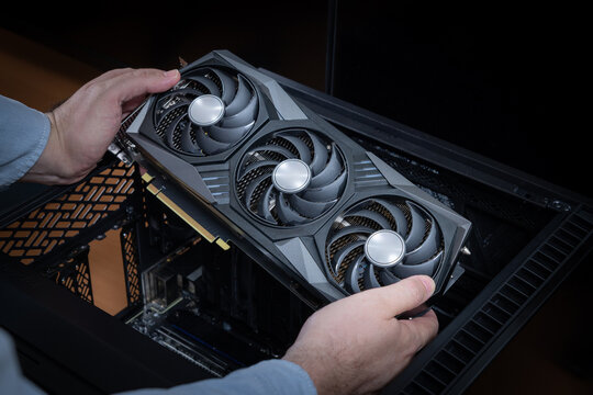 A technician holds a powerful gaming graphics card above an open personal computer case. Expensive computer components. A powerful and expensive PC with scarce components