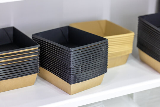 Brown and black rectangular paper food trays stacked neatly, realistic style, on a white shelf background. Concept of food packaging