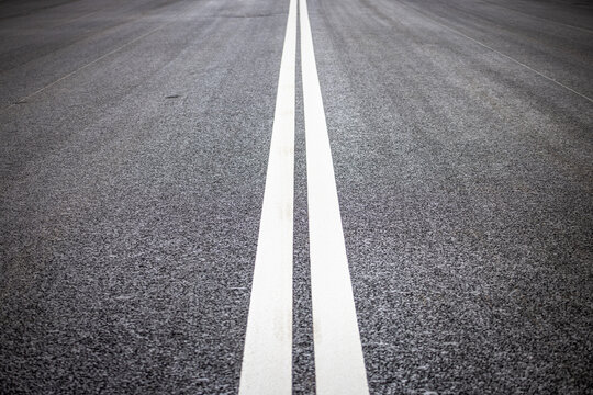 Perspective view of double white solid lines on new asphalt road surface. Symmetric road markings for traffic separation and safety on empty urban highway.