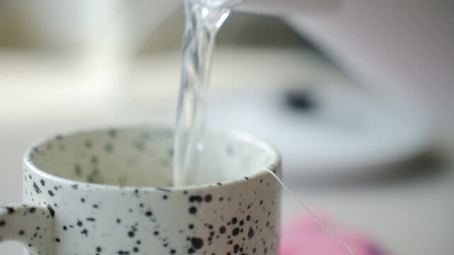 Hand places tea bag in speckled ceramic mug and pours hot water into cup