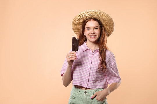 Happy teenage girl with delicious chocolate-glazed ice cream on beige background
