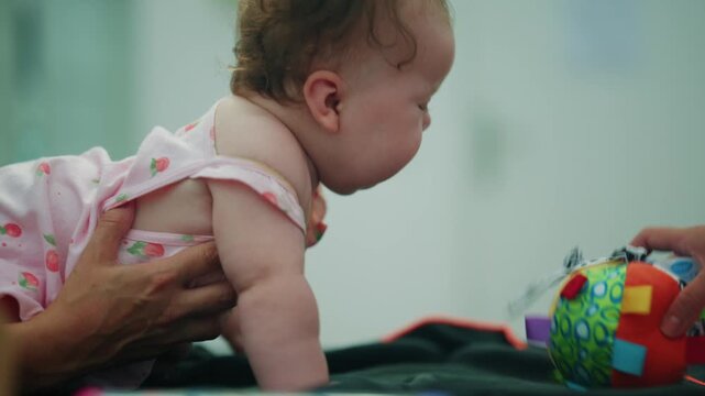 Baby girl on belly interacting with a colorful soft toy ball, developing motor skills during early childhood