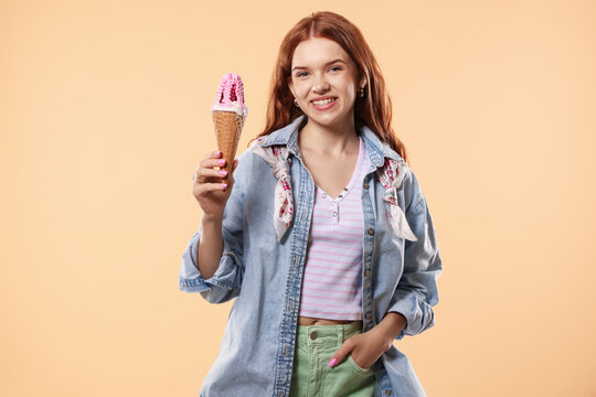 Happy teenage girl with delicious ice cream in waffle cone on beige background