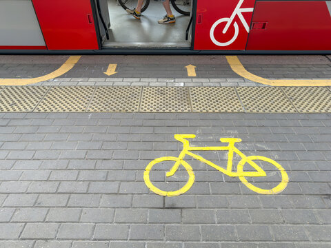 Bicycle sign on public transport platform with red tram doors and passenger legs. Urban mobility concept showing bike transportation rules