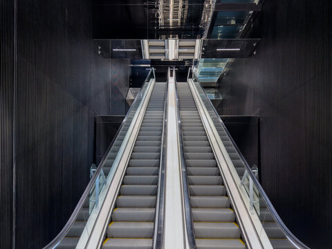 Modern escalator in futuristic dark interior with black ribbed walls and symmetrical design. Contemporary architecture showing moving stairs in a business center or subway station