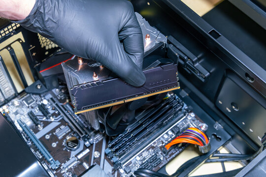 Technician installs a black DDR memory module into a DIMM slot on a motherboard. Assembly or upgrade of a modern PC. Expensive PC components