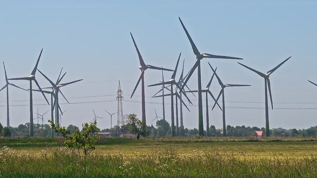 Wind turbines producing renewable green energy rotating in a large wind farm on a sunny day with clear blue sky in emden, germany
