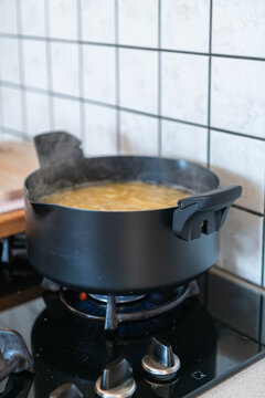 Pot of boiling spaghetti on a gas stove with visible steam and blue flame in a modern kitchen