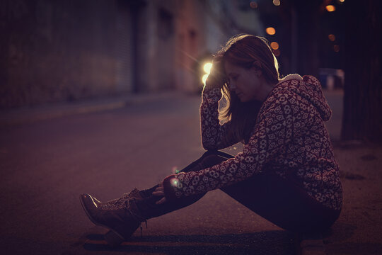 Side view of a mature Woman in despair sitting on the pavement at night