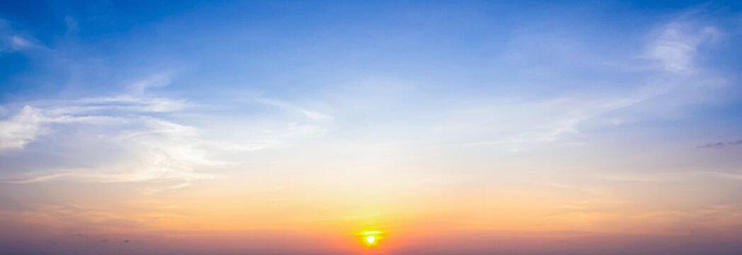 Beautiful sunset sky background with small sun disk on horizon and soft pastel orange light under vibrant blue azure clouds for panoramic travel design