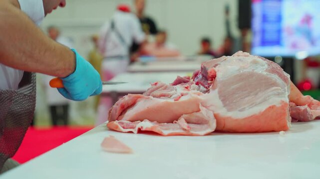 Butcher in protective gear deboning a large cut of raw pork