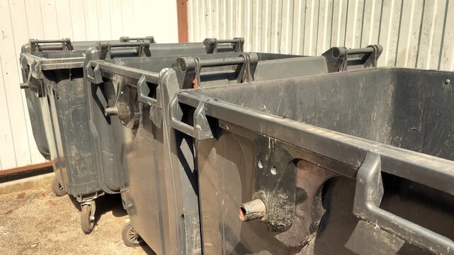 A row of black public municipal trash containers stands outdoors, urban sanitation, waste collection, city maintenance, environmental management.