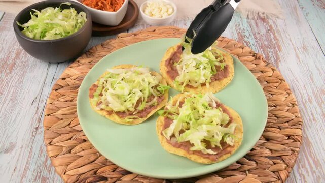 Mexican Tostadas Preparation. Hand prepares a Mexican tostada with fresh lettuce