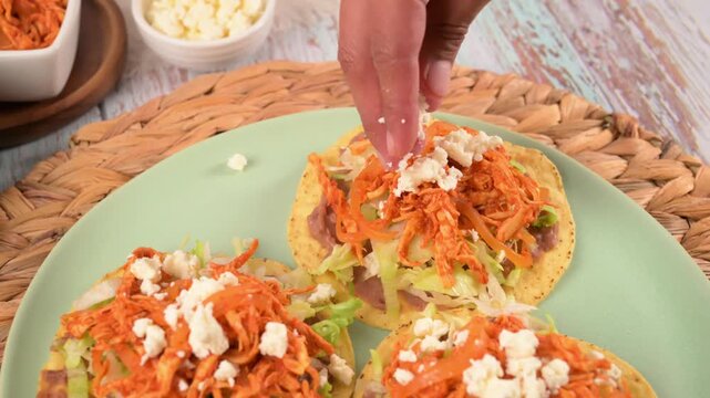 Preparing authentic Mexican tostadas de tinga with shredded chicken and cheese