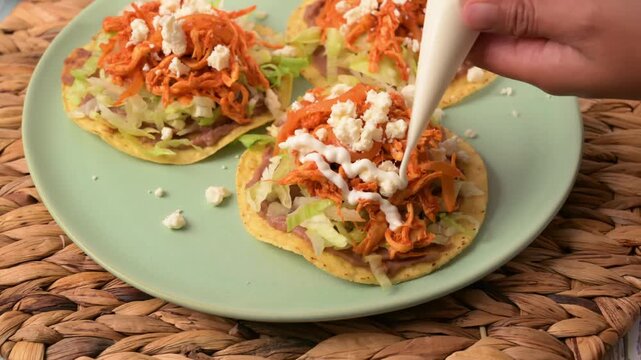 Preparing Mexican food. Adding sour cream to traditional Mexican chicken tostadas