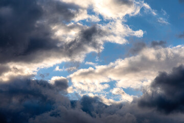 Obraz premium Dramatic dark storm clouds parting to reveal patches of blue sky and sunlight, creating a moody atmospheric weather scene