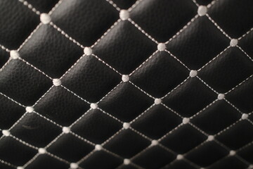Obraz premium Close-up of black textured leather featuring a decorative diamond pattern formed by white contrast stitching. Each intersection has a raised point.