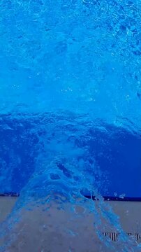 Hydromassage water jet creating bubbles in a clear blue swimming pool. Top view.