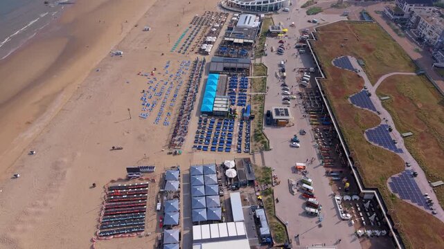 Aerial wide angle view of Scheveningen beach promenade with modern green rooftop solar panels beachfront restaurant complexes and sandy shore under a bright summer sky