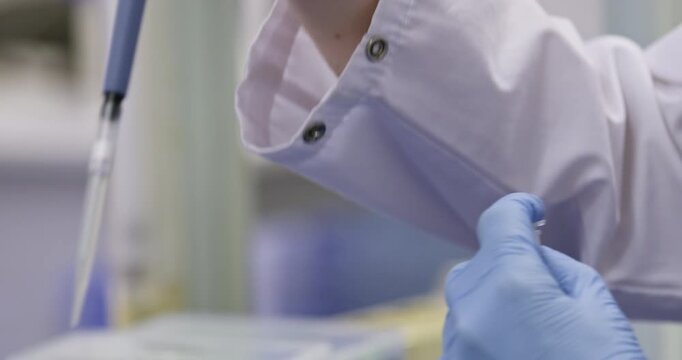 Close-up of a scientist pouring excess liquid from a test tube into a yellow container using a pipette with a tip.