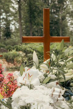 Wooden Christian cross rising above white funeral flowers