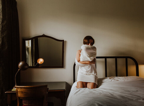 Woman sitting on bed covering face with her dress