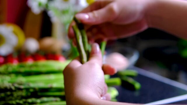 Female hand trimming fresh asparagus by snapping off tough ends before cooking preparing tender green spears for healthy homemade meals and simple recipes