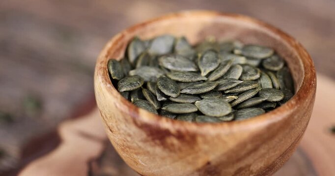 a large number of peeled green dried pumpkin seeds are lying on a wooden walnut board and in wooden dishes, a large number of healthy large pumpkin seeds without shells are ready for cooking