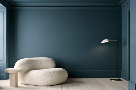 Rounded cream boucle lounge chair sits against a chalky peacock blue paneled wall beside a pale travertine side table and slender brass floor lamp, with light wood boards and broad empty wall space